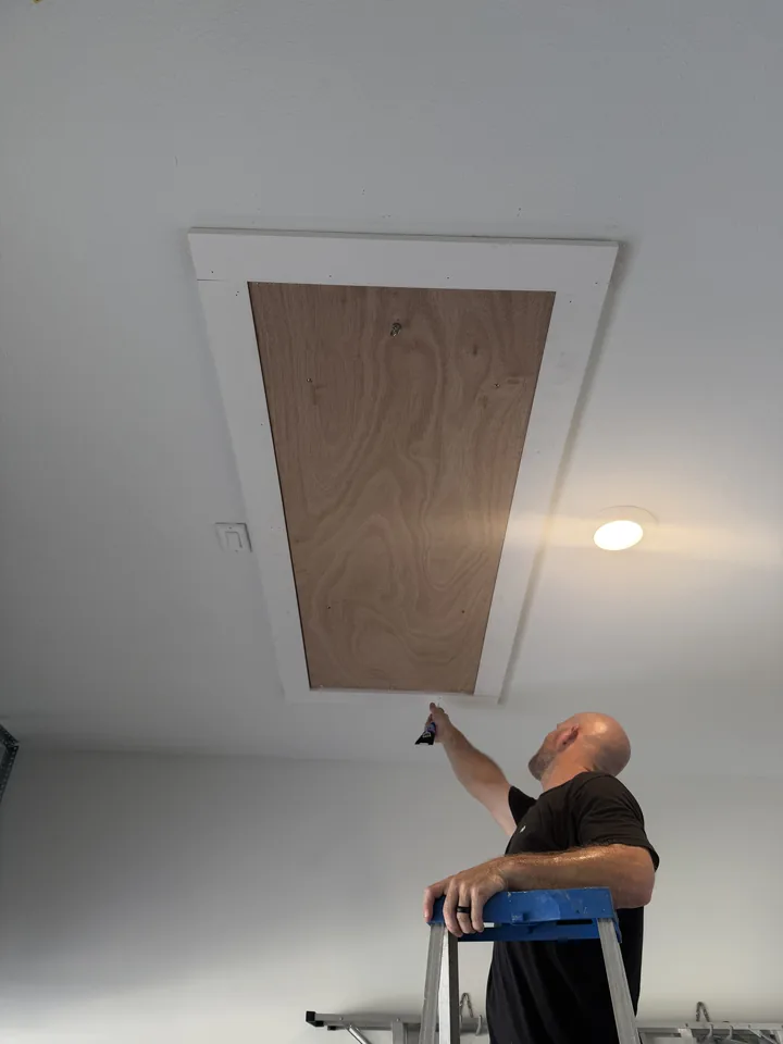An installer on a step ladder checking the new ladder door where it sits in the ceiling trim