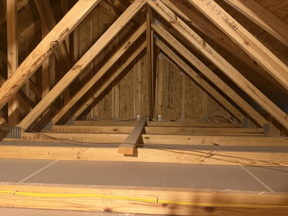 SilverLeaf garage attic before decking: open roof trusses with only a narrow strip of board near the hatch